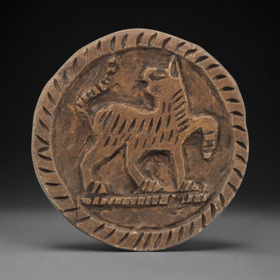 Ancient Steatite Plaque - Near Eastern Feline Relief, 38ZY: Carved from steatite, this circular plaque features a relief depiction of a feline creature, rendered in a stylized, schematic manner. The animal is shown standing in profile, with incised linear deta