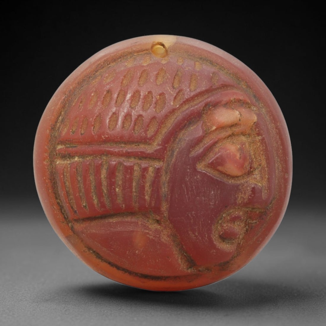 Ancient Carnelian Agate Amulet - Near Eastern Bust Pendant, 43ZX: Carved from carnelian agate, the amulet is a circular disc with a drilled suspension hole at the top, crafted in the ancient Near Eastern style. The front surface bears a raised relief portrait of a h