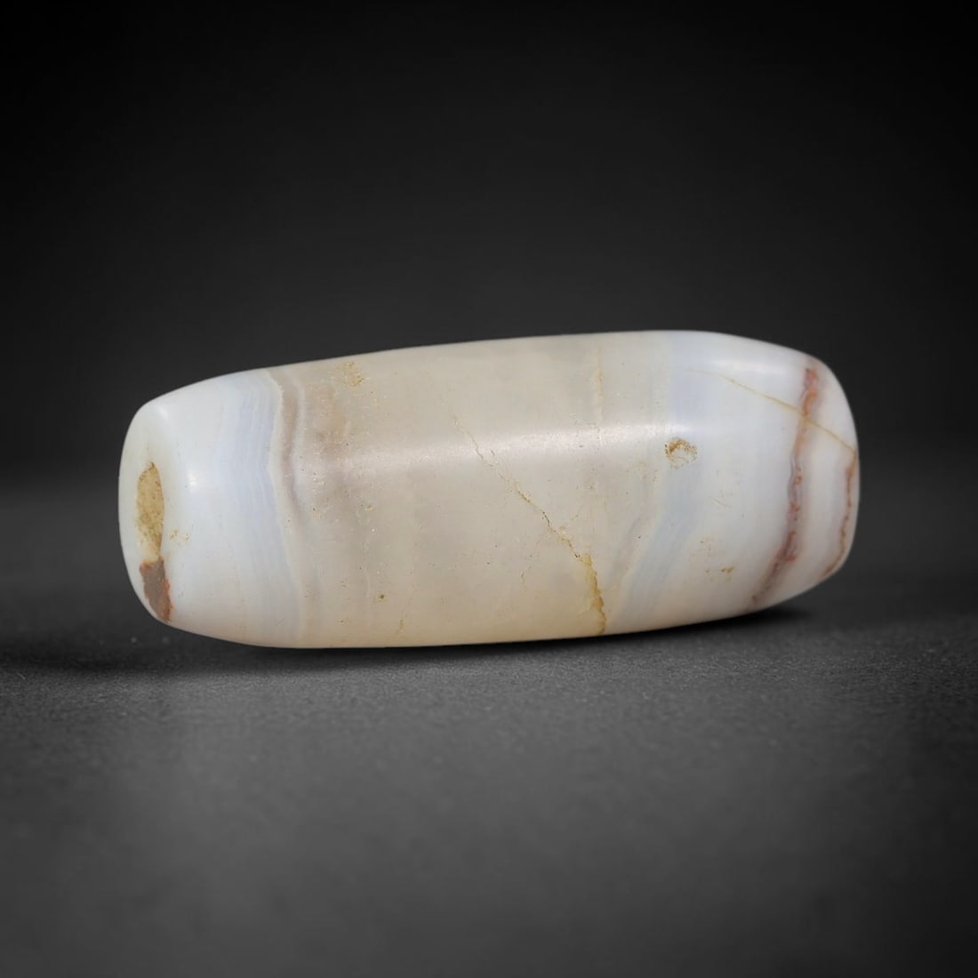 Ancient Banded Agate Bead - Indus Valley Artifact, 80BD: This artifact is crafted from natural banded agate, shaped into an elongated barrel form with soft cream, grey, and subtle reddish-brown concentric banding. The bead features a central perforation for