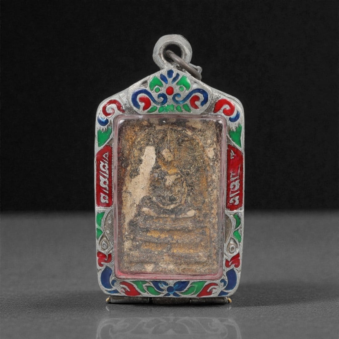 A Thai Buddha Amulet with Silver Frame, 20th Century, 36FP: The amulet is of rectangular form with a pointed upper edge. The obverse features a molded seated Buddha figure in meditative pose (dhyana mudra), rendered in a light-colored material against a tan gr