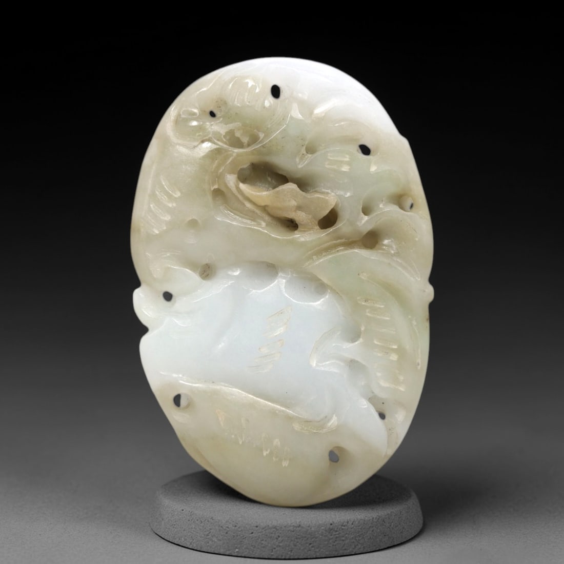 A Chinese Jadeite Jade Openwork Pendant Plaque, 20th Century, 39FR: Carved from pale white to greenish jadeite jade with natural brownish inclusions and subtle veining, the pendant is formed as an oval plaque with a scalloped edge, intended for use as an amulet pendan