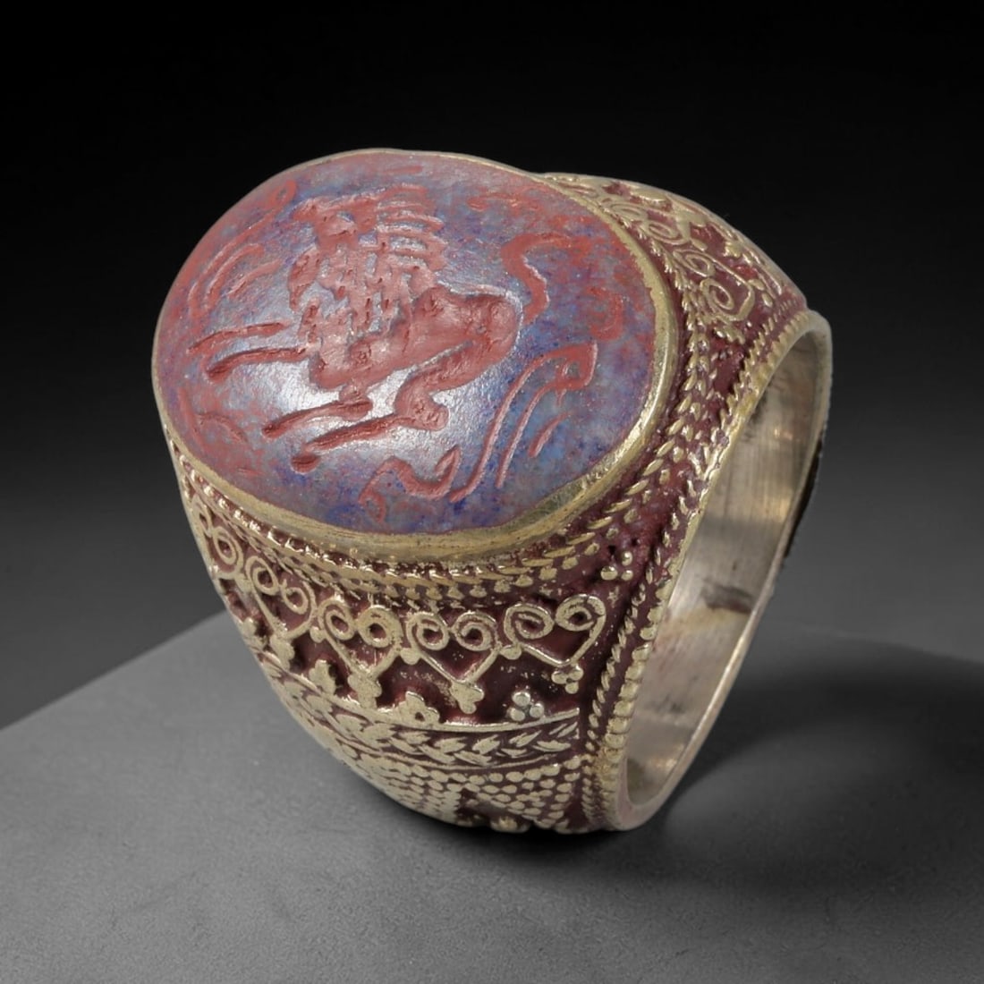 Antique Silvered Ring - Eurasian Steppe Intaglio Carnelian Cabochon, 87BH: Silvered metal ring featuring a carved carnelian intaglio cabochon set into the bezel, depicting a stylized equine figure with intricate detailing. The band is adorned with pseudo-filigree wirework, r