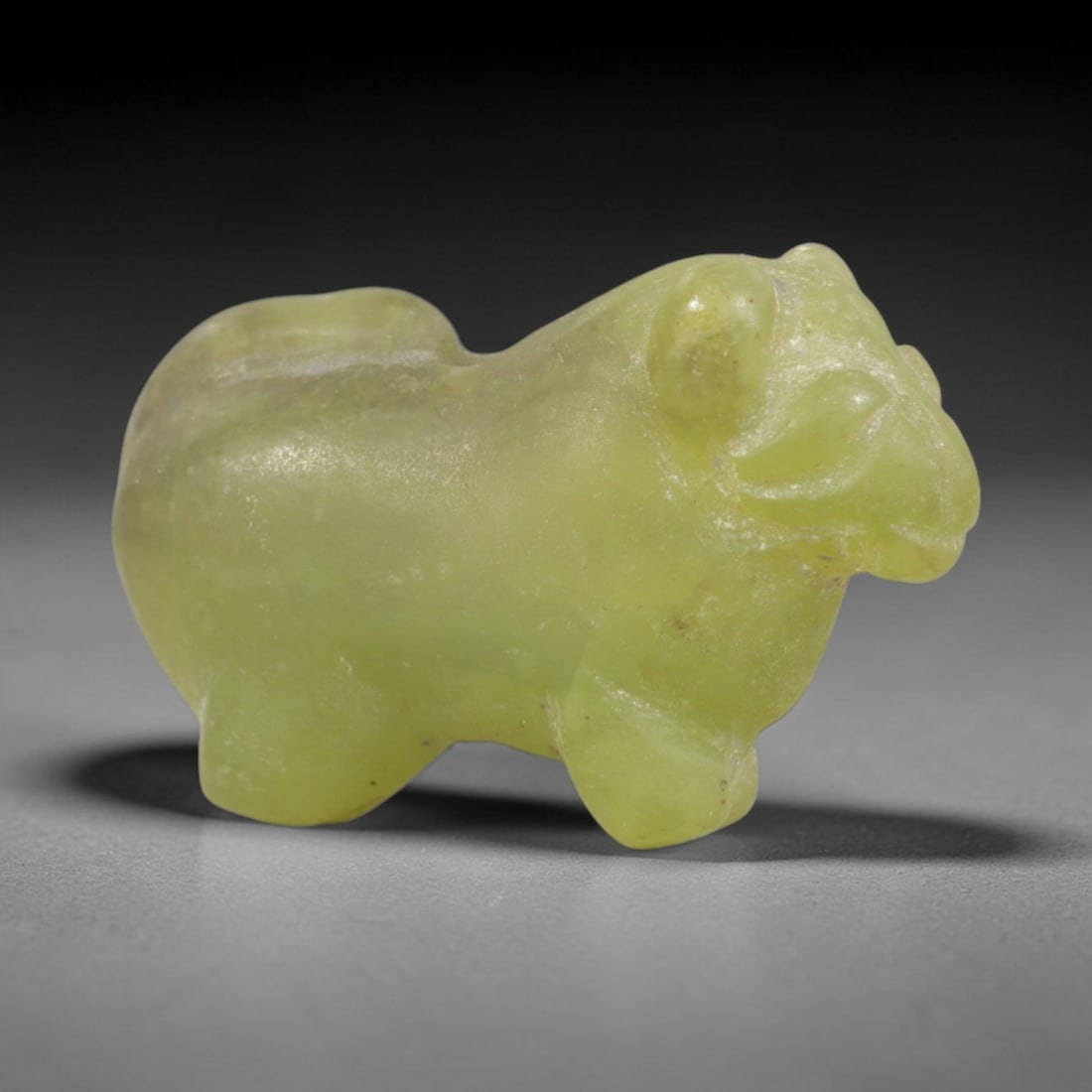 Ancient Serpentine Bovid - Egyptian Animal Figurine, 52AR: This artifact is carved from pale, translucent green serpentine, exhibiting a smooth, polished surface with subtle natural inclusions and faint surface wear consistent with age. The form is a stylized