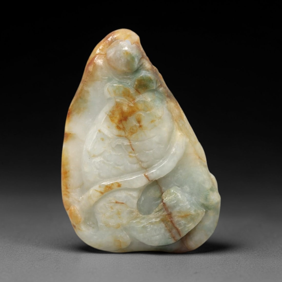 A Chinese Jadeite Jade Fish-Form Pendant Plaque, 20th Century, 14FR: Carved from predominantly white jadeite jade with prominent honey-brown and celadon inclusions, the pendant is formed as an irregularly shaped, tapered plaque. The surface is executed in high relief t