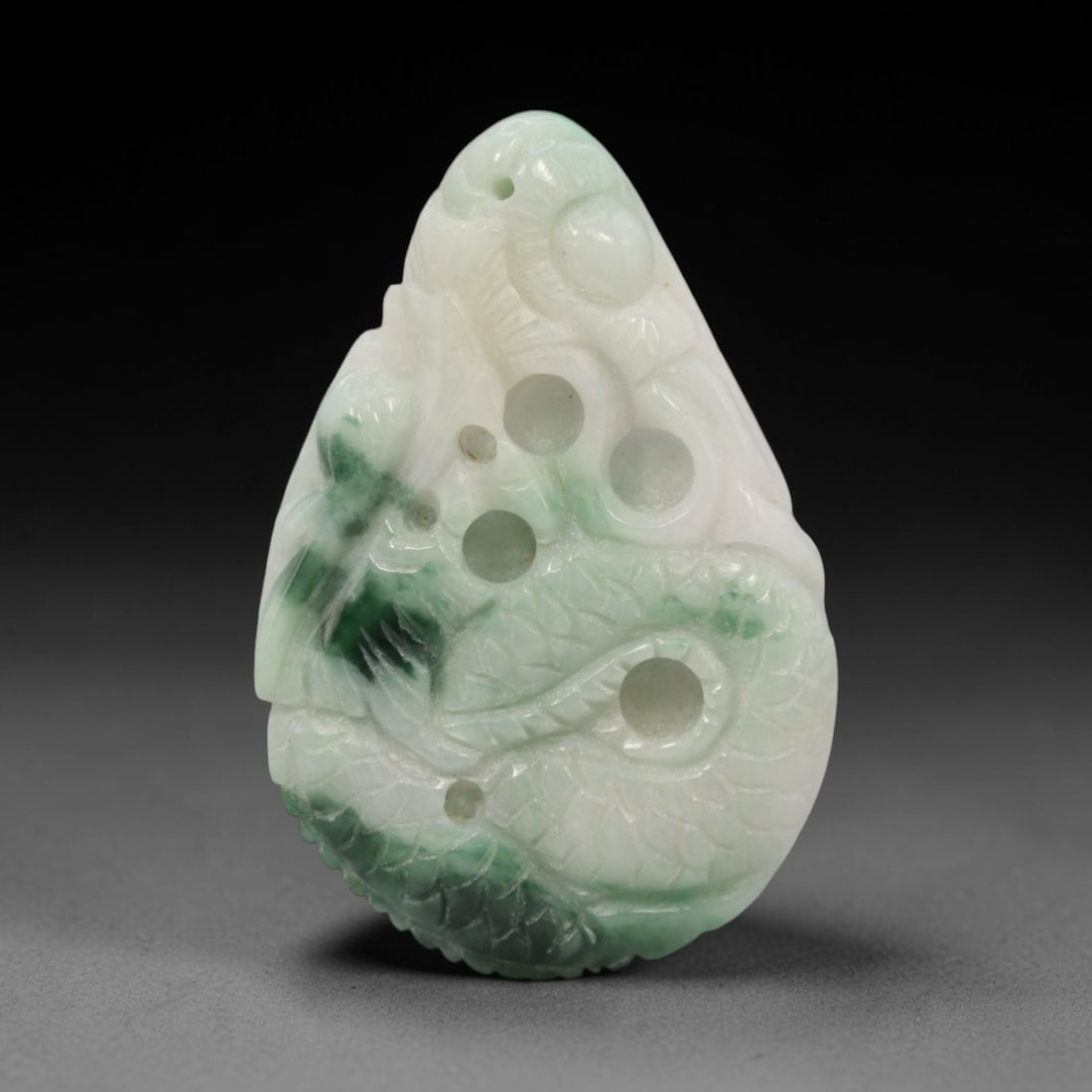 A Chinese Jadeite Jade Dragon Pendant, 20th Century, 9ZL: Carved from white jadeite with prominent green inclusions, the object is formed as a teardrop-shaped pendant. The front is decorated in openwork relief with a coiled dragon, featuring incised scale pa
