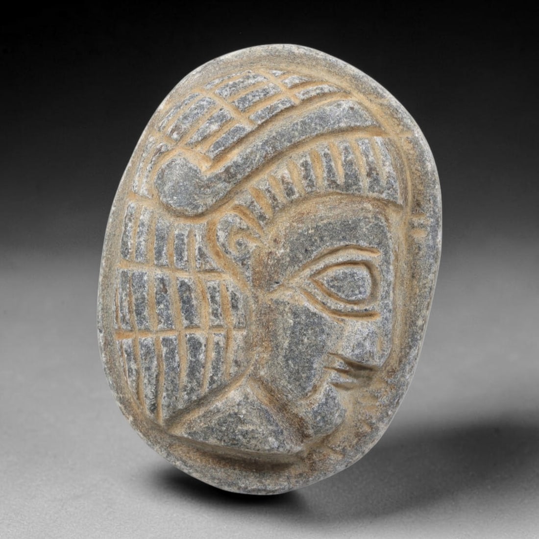 Ancient Stone Amulet - Near Eastern Bust Plaque Pendant, 52FY: Carved from dark stone, the amulet is an oval plaque crafted in the ancient Near Eastern style, featuring a raised relief portrait of a human bust in profile. The surface bears incised details renderi