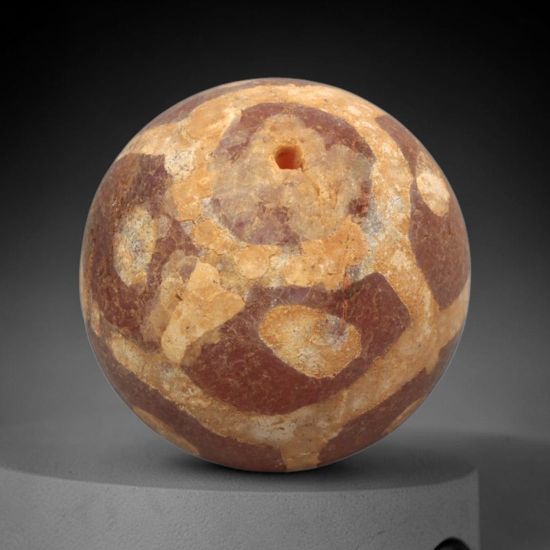 Ancient Carnelian Etched Bead - Gandhara Spherical Bead, 23XY: The bead is carved from carnelian, a semi-precious chalcedony, with a spherical form and a laterally drilled suspension hole. Its surface features an etched white geometric pattern of circular and ang
