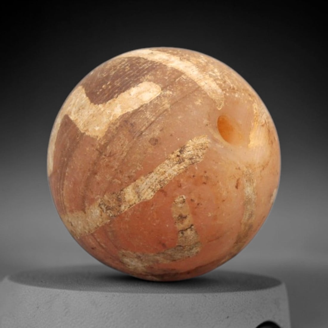 Ancient Carnelian Etched Bead - Gandhara Spherical Bead, 58XY: The bead is crafted from carnelian, a semi-precious chalcedony, with a spherical form and laterally drilled suspension hole. Its surface features an etched white pattern of angular and banded geometri