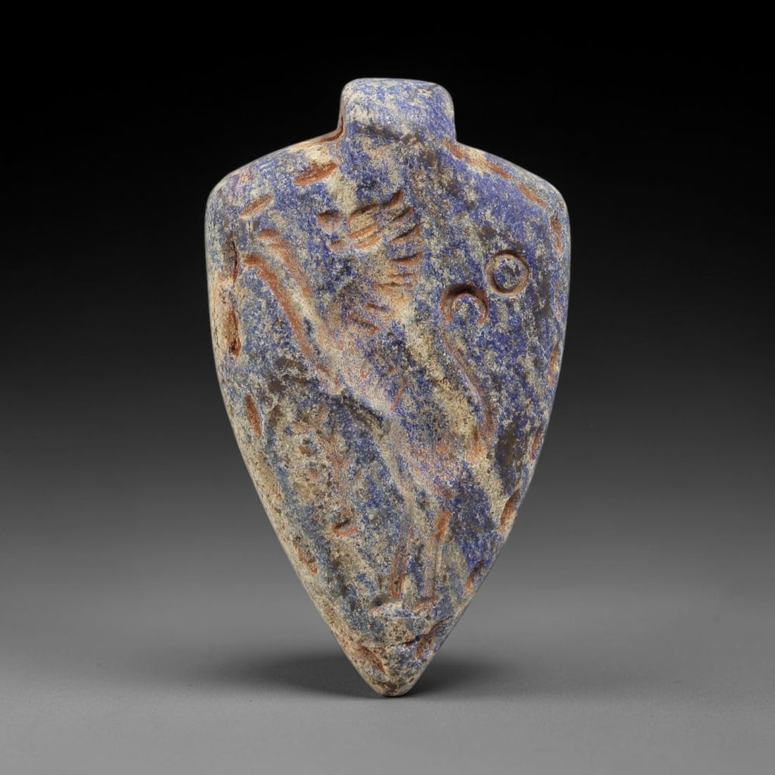 Ancient Lapis Lazuli Amulet - Near Eastern Animal Figurine, 42BA: Carved from lapis lazuli, the amulet takes a teardrop-shaped form with a suspension loop at the top, designed for wear as a protective talisman. The front face is incised with a stylized quadruped ani