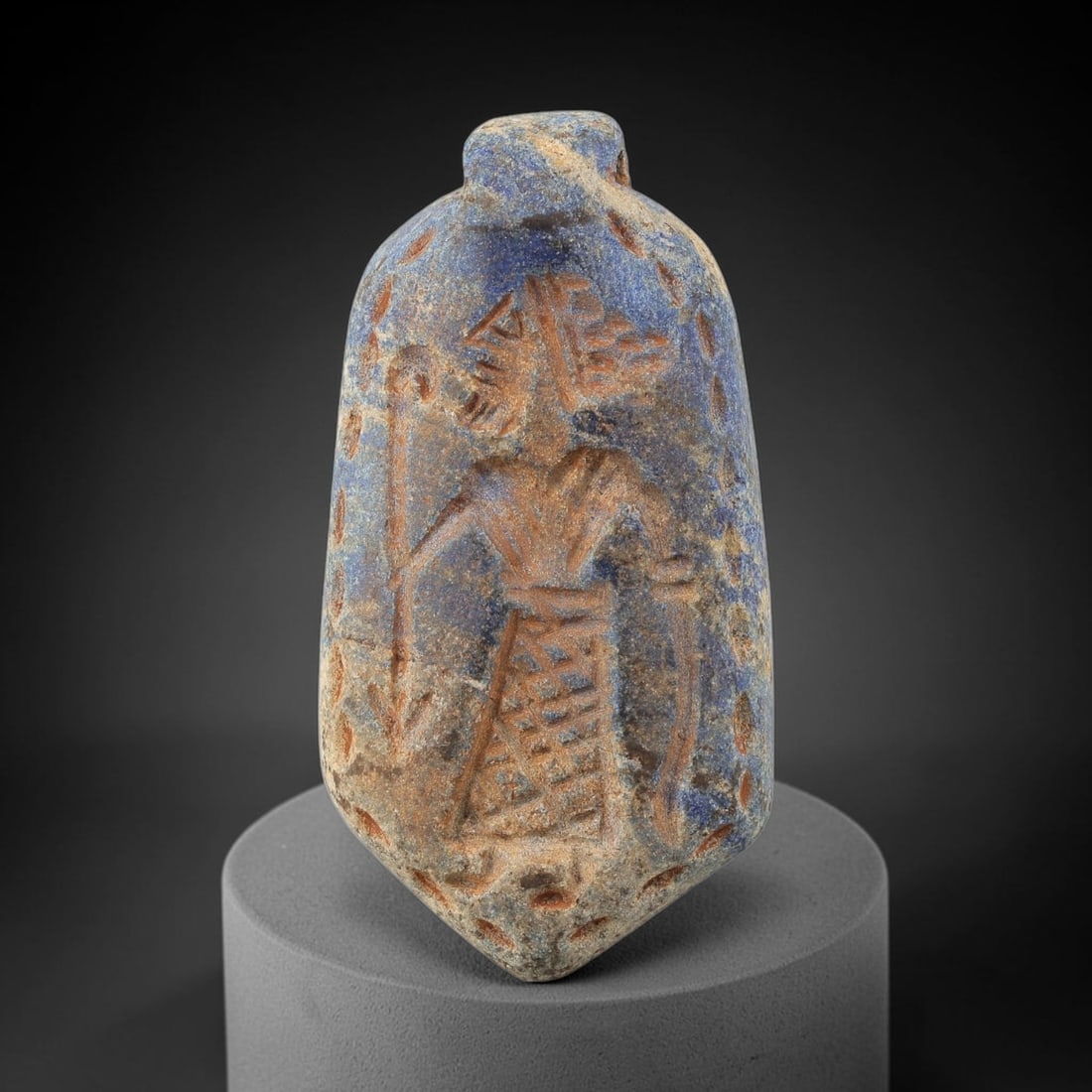 Ancient Lapis Lazuli Amulet - Near Eastern Figurine, 10BA: Carved from lapis lazuli, the amulet takes a lozenge-shaped form with a suspension loop at the top, designed for wear as a protective talisman. The front face is incised with a standing anthropomorphi