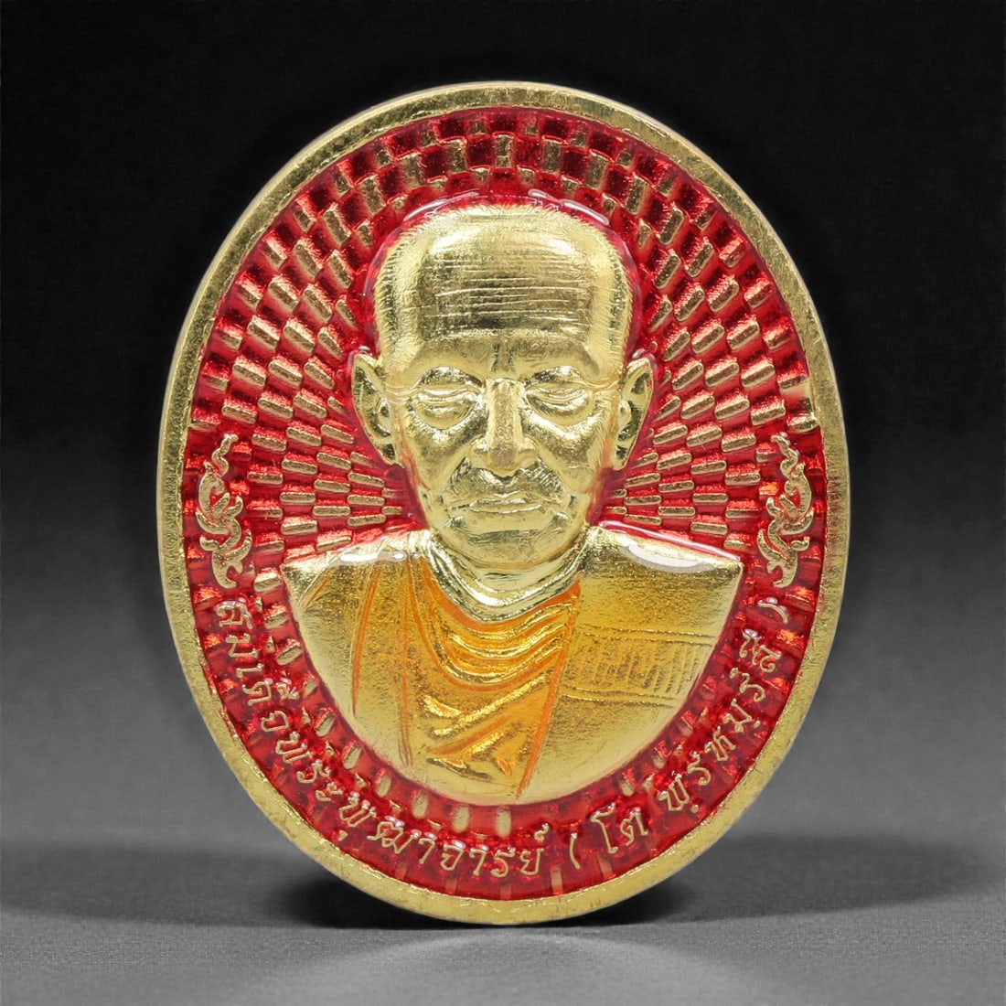 A Thai Gilt-Metal and Enamel Monk Portrait Medallion, 21st Century, 88FP: Cast from metal with a gilt surface finish, the medallion is oval and double-sided with a raised gilt-metal border. The obverse features a high-relief gilt bust portrait of a Buddhist monk, set agains