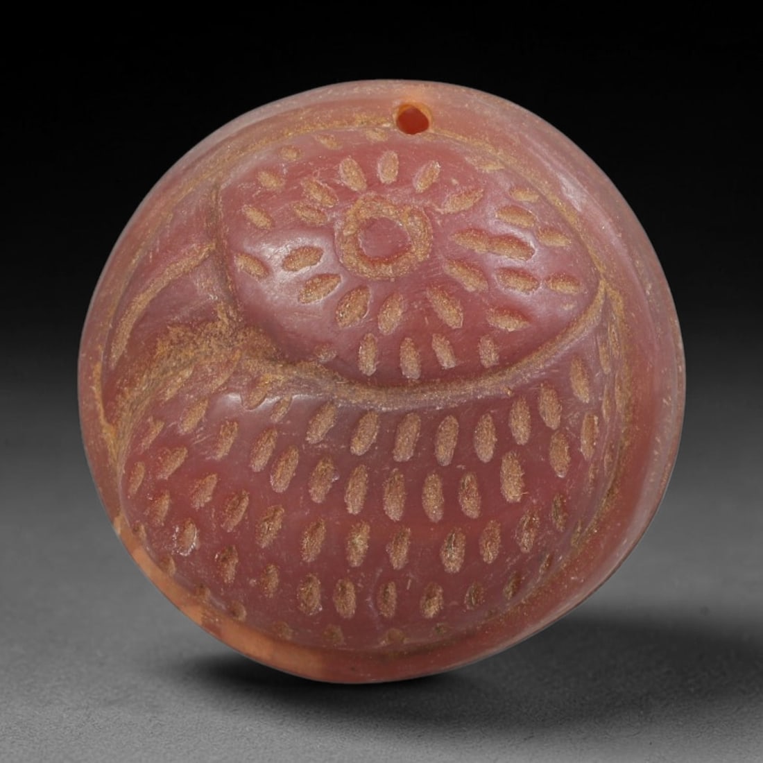 Ancient Carnelian Amulet - Near Eastern Bird Head Pendant, 59FY: Carved from carnelian, the amulet is a circular disc with a drilled suspension hole at the top edge, crafted in the ancient Near Eastern style. The front surface bears a raised relief bird head motif,
