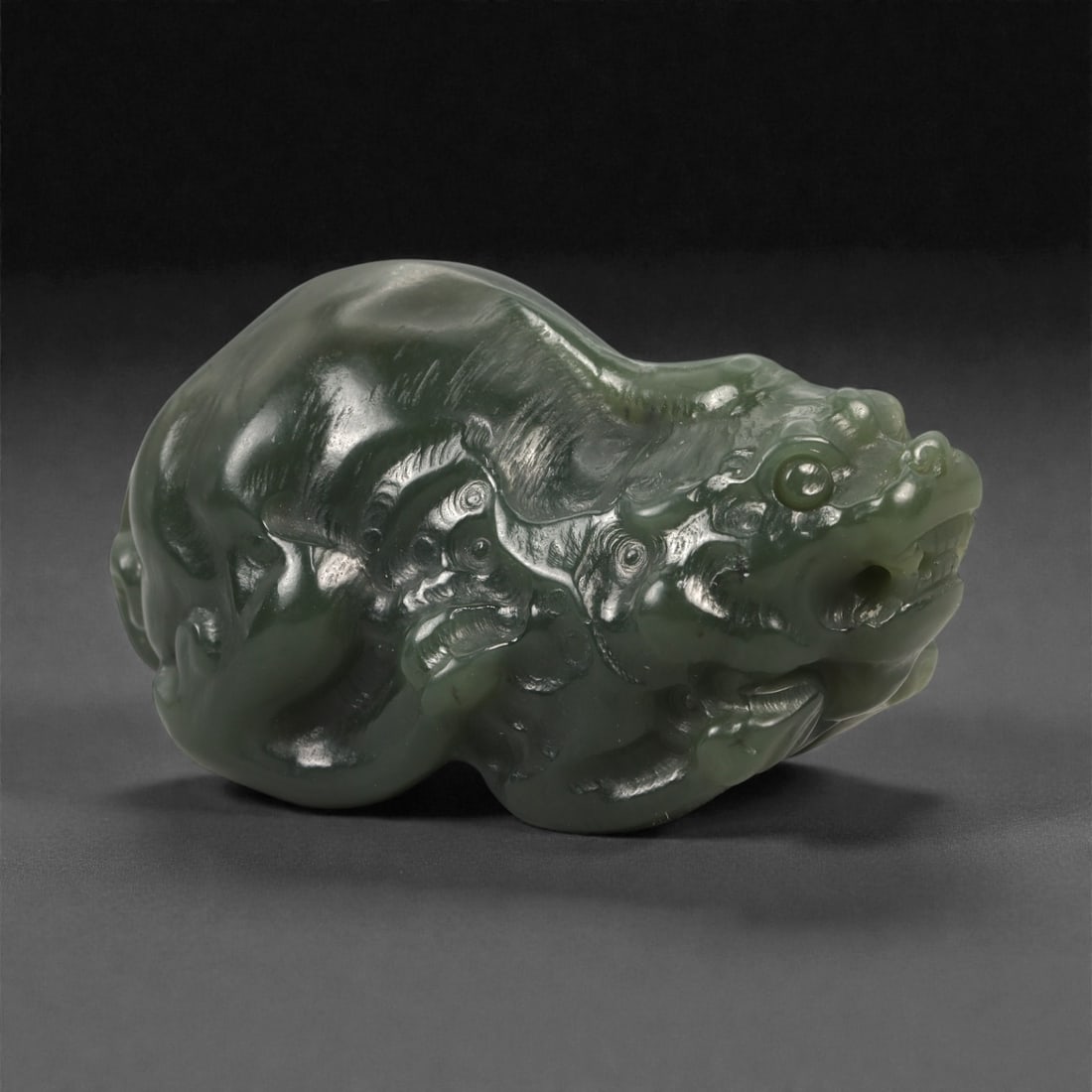 Chinese Dark Green Jade Pi Xiu - Guardian Beast Figurine, 88ZD: Carved from dense, dark green jade with a high-polish finish, this compact sculptural figure depicts a pi xiu in a powerful crouching posture. The mythical creature is rendered with a pronounced drago