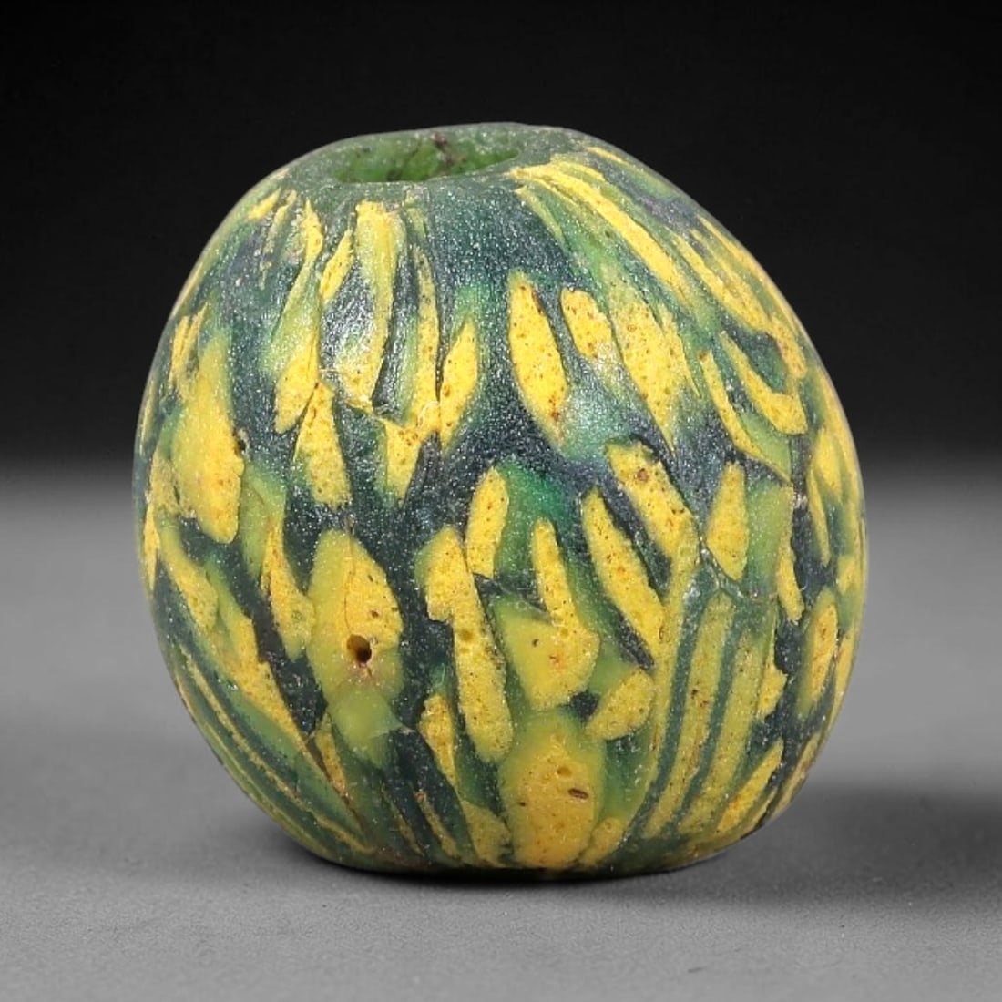 Ancient Glass Bead - Roman Mosaic Spherical Pendant, 35BG: A spherical ancient glass bead crafted using the mosaic glass technique, with a deep green glass base adorned with irregular, slab-like motifs in bright yellow. The surface features a textured, heavil