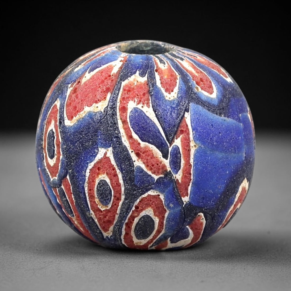 Ancient Glass Bead - Roman Millefiori Eye Bead Pendant, 42BG: A spherical ancient glass bead crafted in the millefiori mosaic technique, with a complex fused cane pattern of repeating concentric eye motifs. The surface features interlocking designs in deep red, 