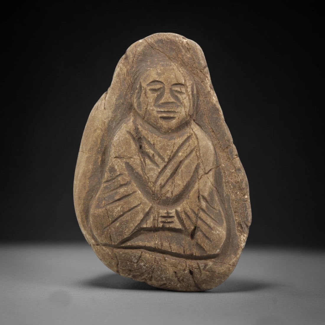 Antique Stone Relief Carving - Japanese Edo Period Seated Figure, 55BH: A carved stone relief of irregular pebble form, fashioned from a single piece of weathered sandstone with a warm tan patina. The front is carved in deep relief to depict a seated figure in traditional