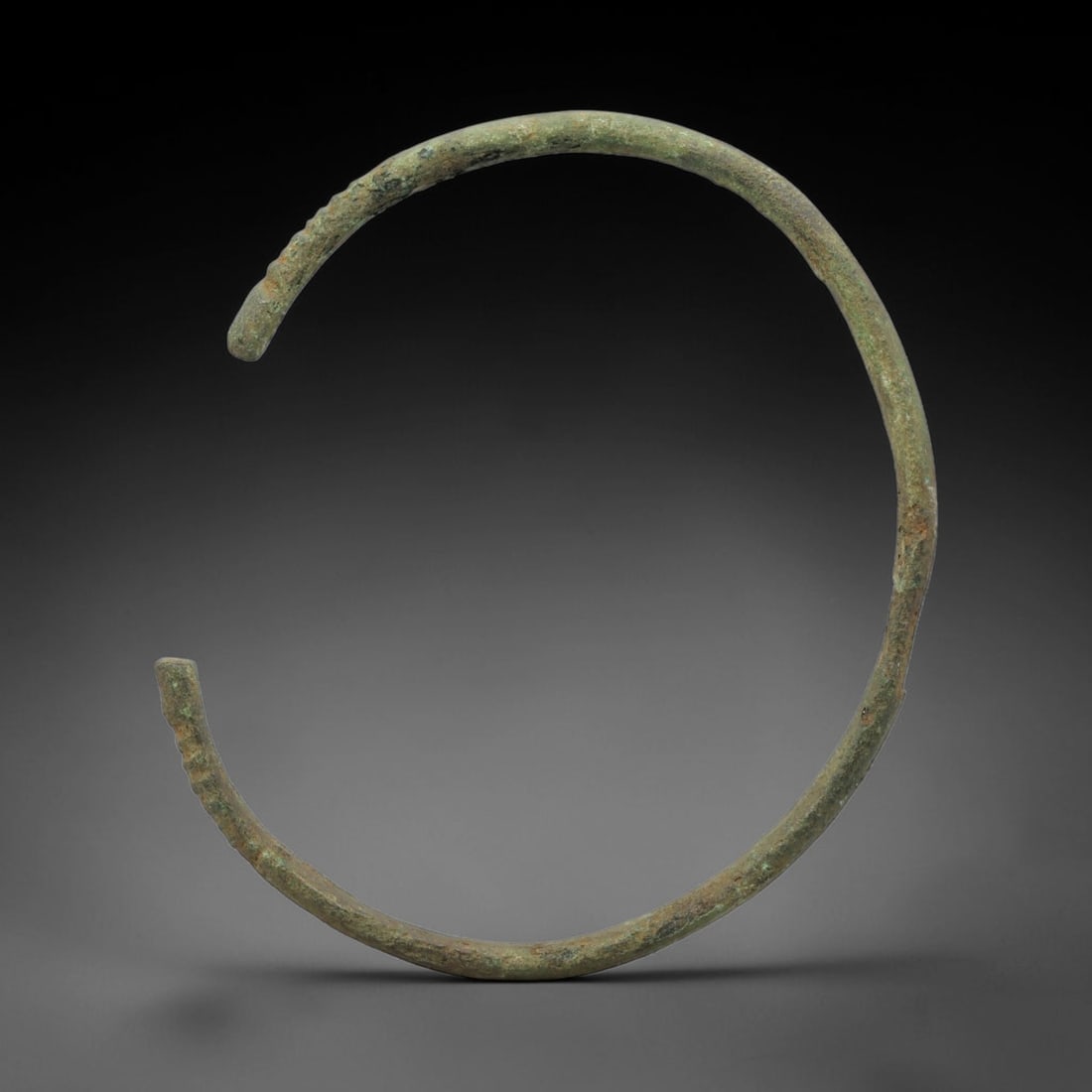 Ancient Bronze Bracelet - Roman Decorated Armlet, 24BH: A cast bronze open-cuff bracelet of circular form, crafted from a single continuous bronze band with an open terminal design for wear. The outer surface of the band features incised ribbed decoration 