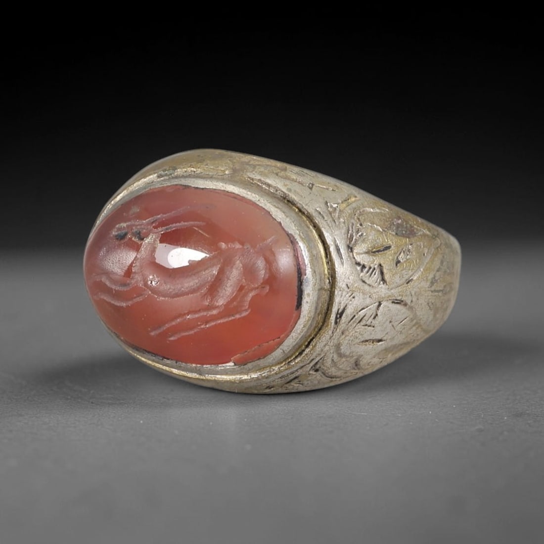 Antique Silvered Ring - Eurasian Steppe Carnelian Gazelle Intaglio, 13BK: Silvered metal ring featuring an oval carnelian cabochon carved with an intaglio depiction of a leaping gazelle, set in a bezel with a partial gilded finish. The band displays hand-engraved decorative