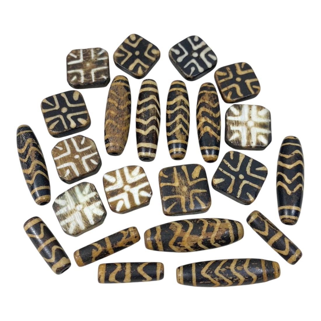 A Lot of 23 Antique Himalayan Etched Pumtek Wood Dzi Beads, 32AC: The group comprises 23 antique etched pumtek wood dzi beads, featuring both barrel-shaped and square forms, with classic Himalayan geometric patterns including zigzag lines, crosses, and star motifs e