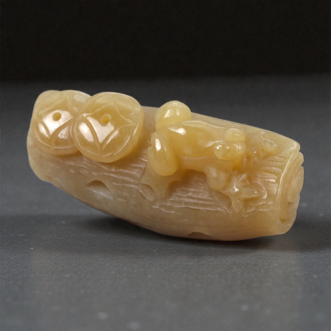 A Chinese Jade Frog and Coin Branch Ornament, 20th Century, 96FA: Carved from pale yellow jade with areas of soft translucency and natural tonal variation, the ornament is worked in the round as a frog and coin group resting on a stylized tree branch. The branch is 