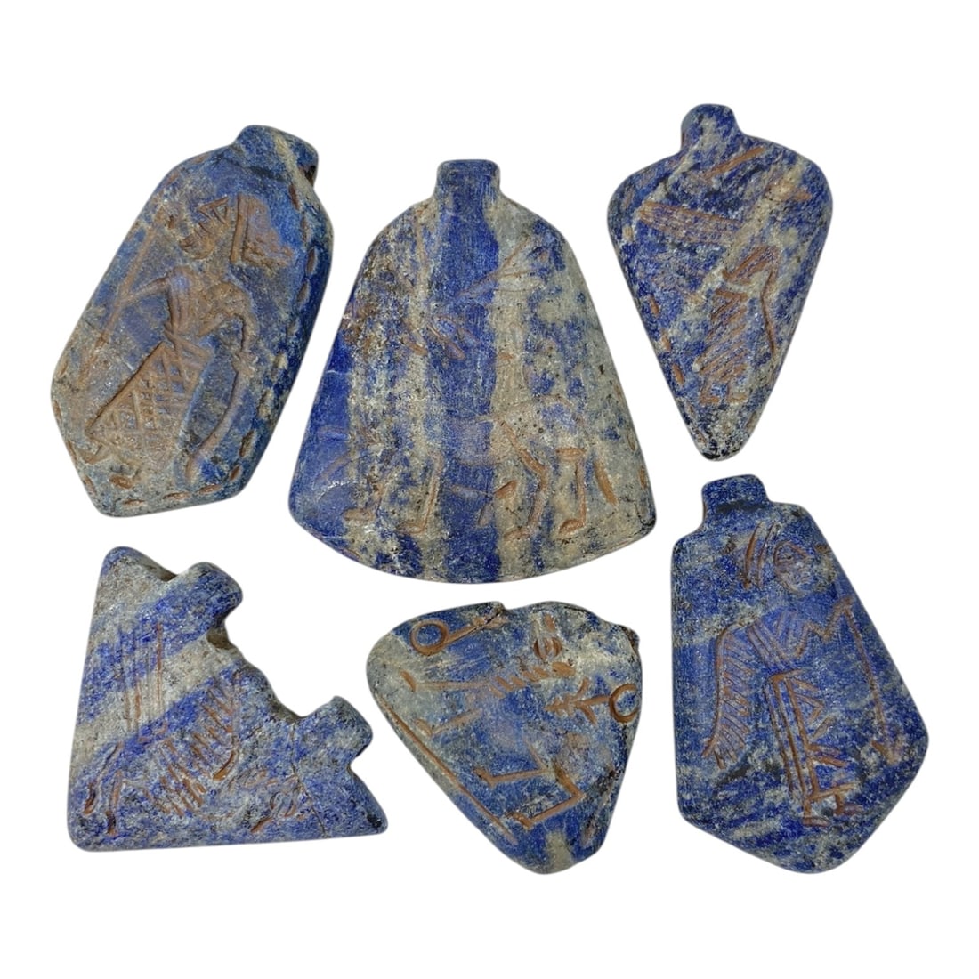 A Lot of 6 Ancient Near Eastern Lapis Lazuli Amulets, 8AC: The group comprises six amulets carved from lapis lazuli, exhibiting varying shades of blue with natural white and grey inclusions and surface patina consistent with ancient wear. Each amulet features