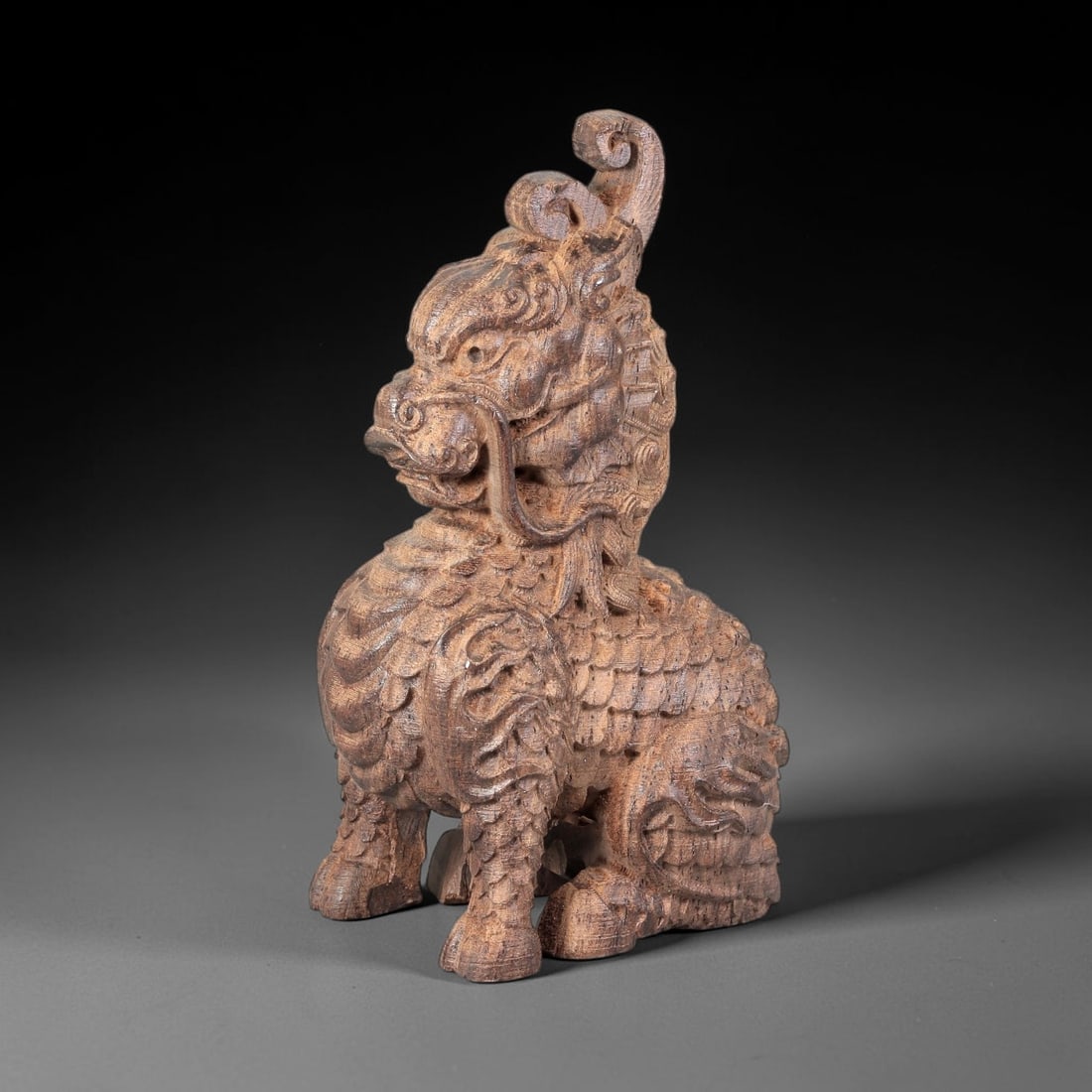 A Chinese Agarwood Qilin Figurine, 20th Century, 50FC: Carved from agarwood with natural tonal variation and a rich brown patina, the figurine depicts a seated qilin (mythical auspicious beast) in the round. The head features a curled, spiraling crest, la
