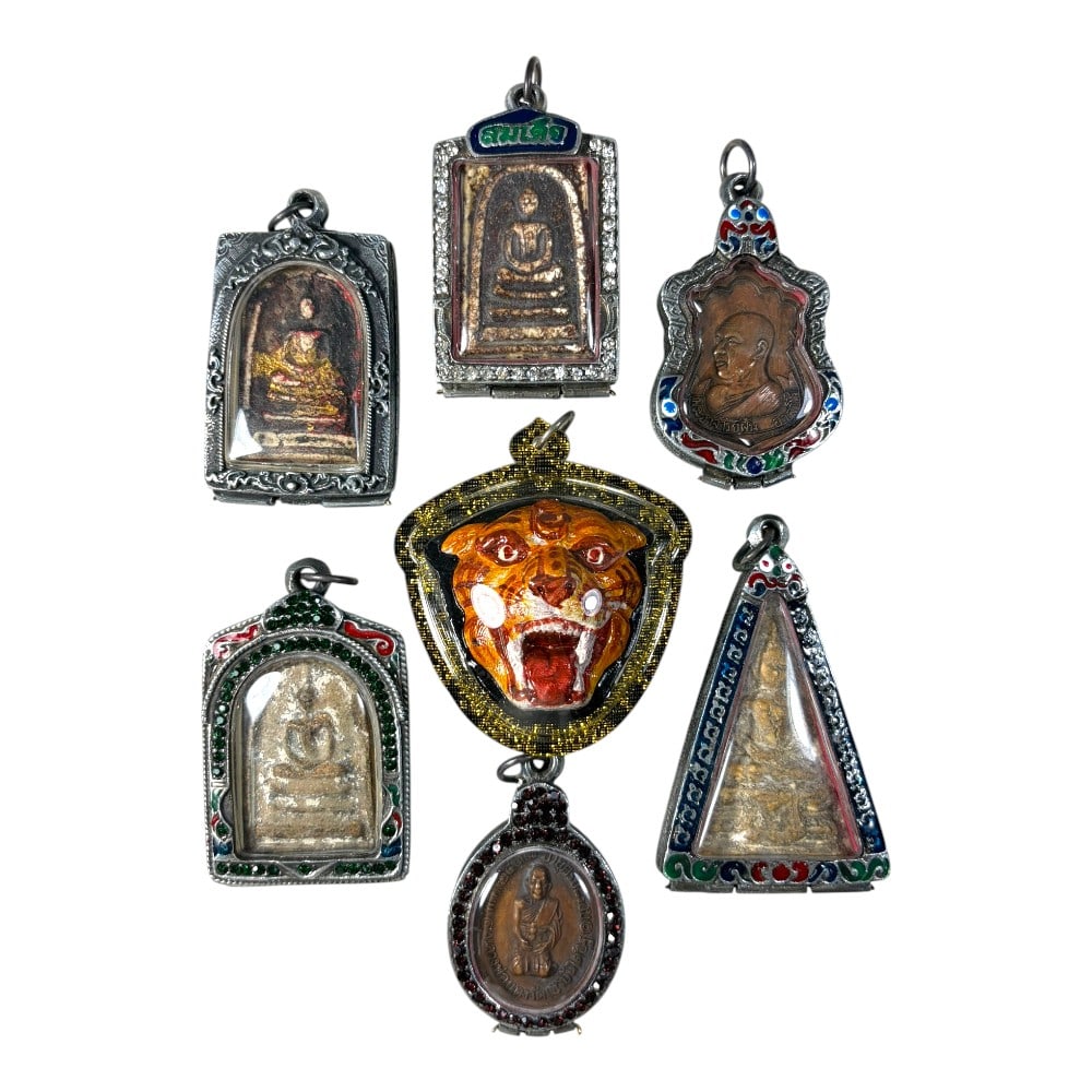 A Lot of 7 Vintage Thai Buddhist Amulets with Enamel and Jewel Accents, 42AA: Comprising seven pendants ranging from 6 to 7 cm in height. The collection features a diverse range of amulets, including seated Buddha figures, monastic portraits, and a striking enamel tiger head am