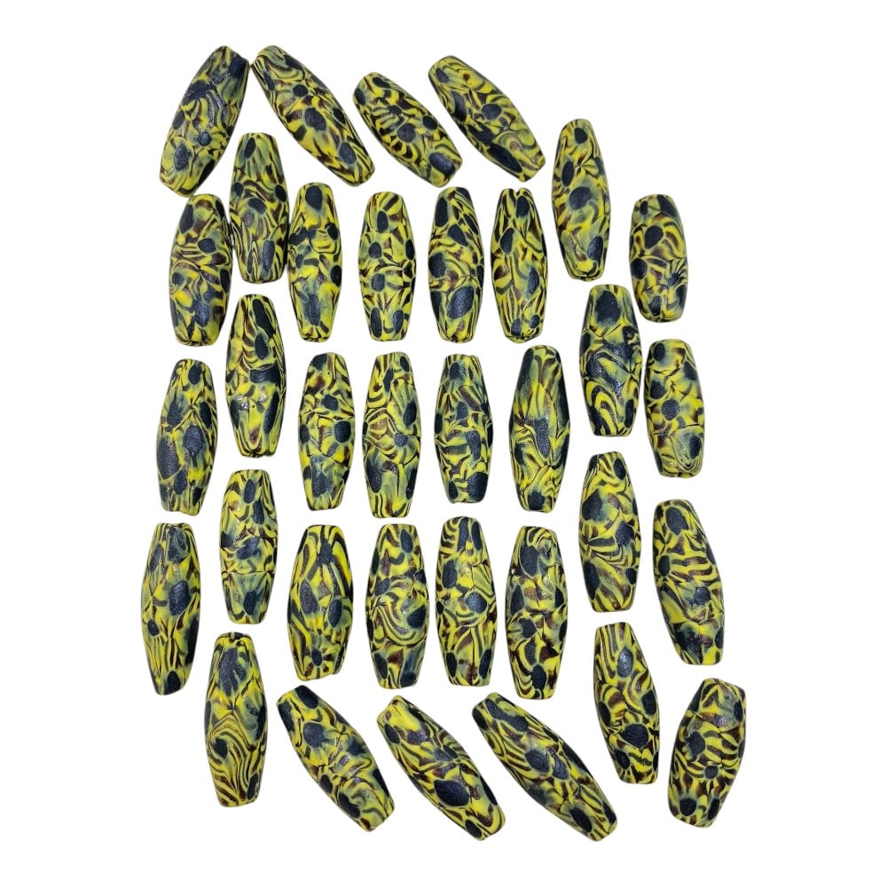 A Lot of 34 Vintage Cylindrical Glass Trade Beads, 75AA: This collection features 34 uniformly shaped vintage glass beads, showcasing a striking, consistent design. Each bead is a long, slender cylinder with a vibrant yellow base, overlaid with black spotte