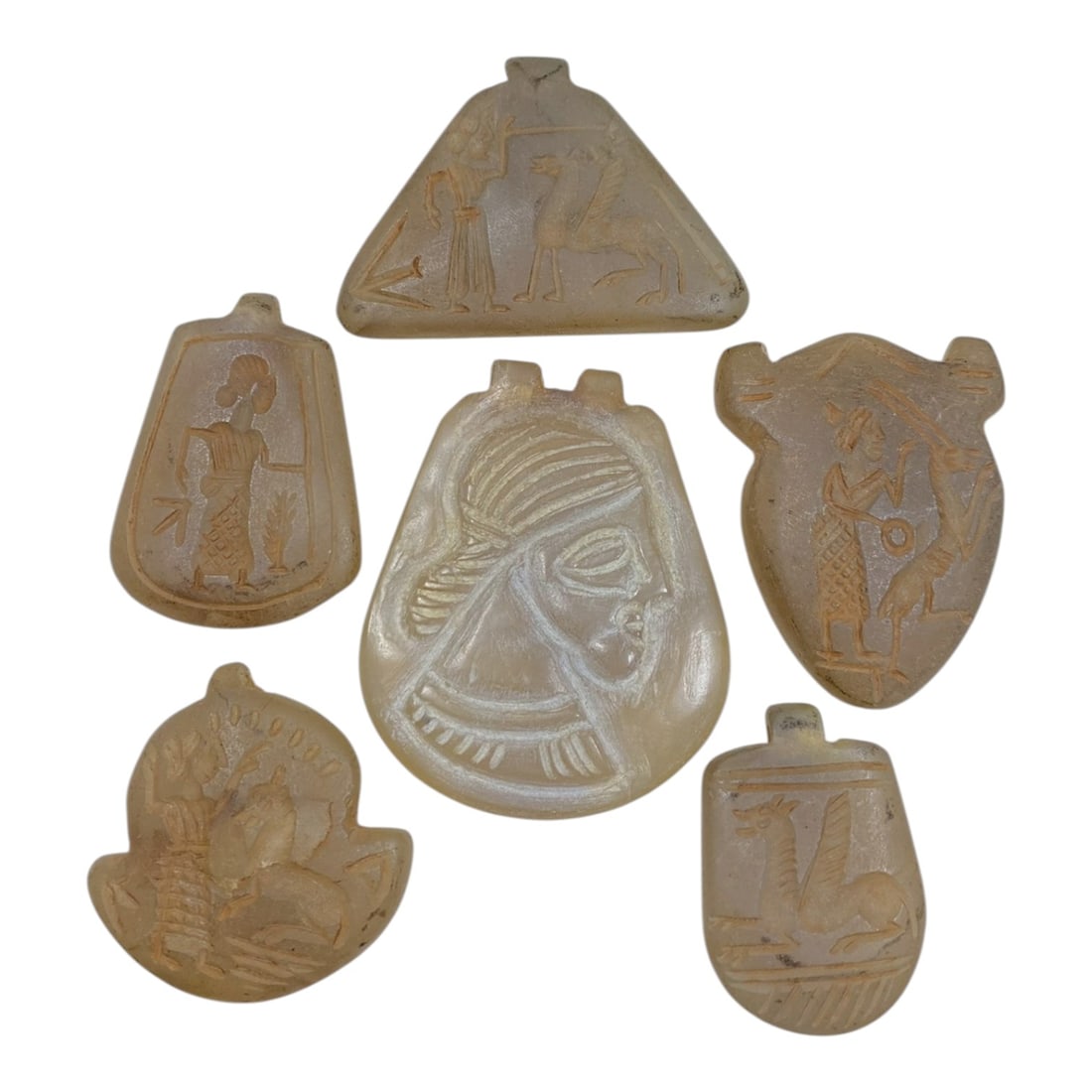 A Lot of 6 Ancient Sasanian Chalcedony amulets, 88AB: The group comprises six ancient Sasanian-style amulets, carved from translucent chalcedony with warm, pale beige tones and age-related patina. Each piece features a distinct shape-including triangular