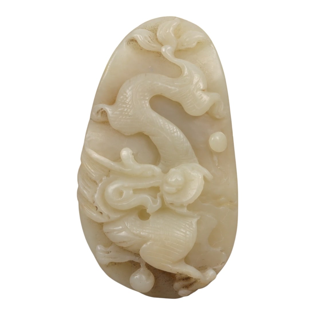 A Chinese Nephrite Jade Dragon Pendant, Qing Dynasty, 78YA: Carved from pale creamy-white nephrite jade, with a smooth, polished surface and subtle natural tonal variations consistent with aged Chinese jade. The pendant is of irregular, rounded-oval form, with