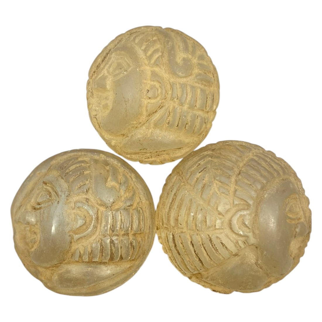 Lot of 3 Ancient Glass Anthropomorphic Relic Beads, 41WK: The lot comprises three spherical glass beads, each featuring deeply carved anthropomorphic human face motifs with stylized features, including eyes, noses, mouths, and patterned hairstyles. The trans