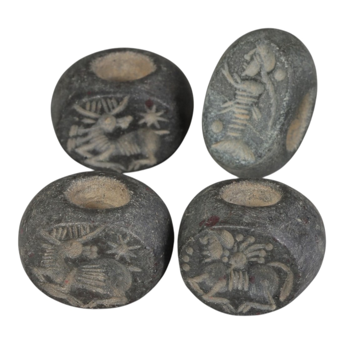 Lot of 4 Ancient Sasanian Stone Stamp Seals, Circa 3rd-7th Century CE, 69WP: A collection of four Sasanian period stamp seals, carved from dark grey stone, each featuring a central drilled hole for suspension. The seals display characteristic Sasanian iconography: including ho
