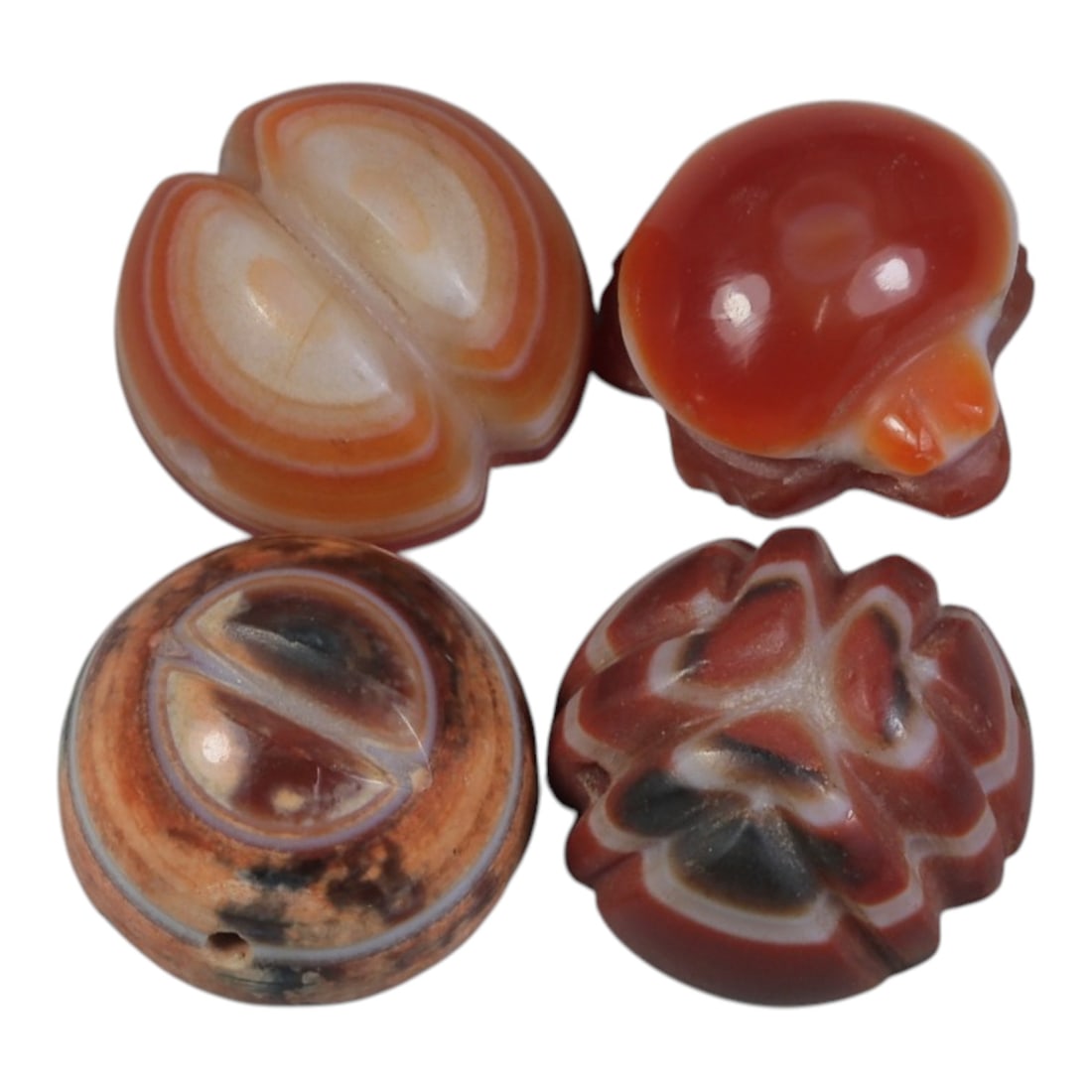 Lot of 4 Antique Himalayan Carnelian Beads, 52WP: A collection of four antique Himalayan carnelian beads, each intricately carved from banded carnelian stone. The beads showcase varied forms and designs: including a double-lobed pattern utilizing nat