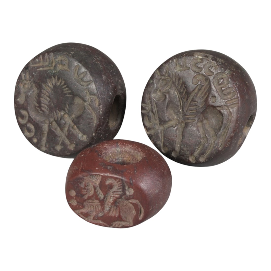 Lot of 3 Ancient Sasanian Stone Stamp Seals, Circa 3rd-7th Century CE, 66WP: A collection of three Sasanian period stamp seals, carved from reddish-brown stone, each featuring a central drilled hole for suspension. The seals display characteristic Sasanian iconography: includi