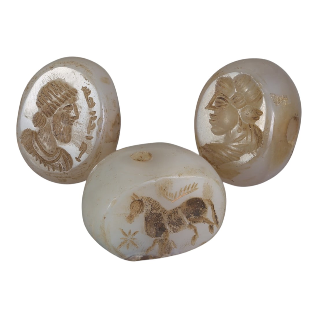 Lot of 3 Ancient Sasanian Chalcedony Stamp Seals, Circa 3rd-7th Century CE, 59WP: A collection of three Sasanian period stamp seals, expertly carved from translucent chalcedony stone, each featuring a central drilled hole for suspension. The seals display characteristic Sasanian ic