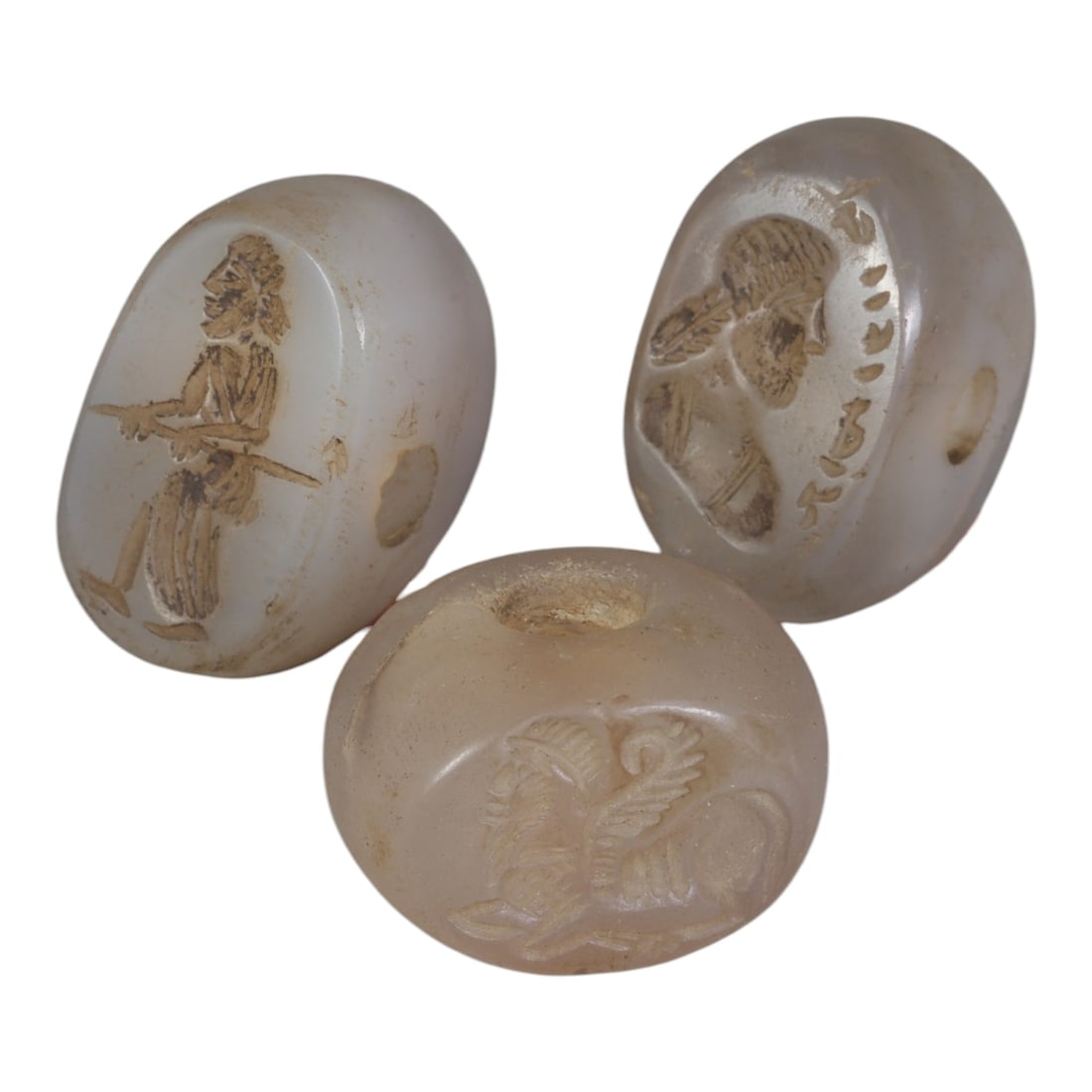 Lot of 3 Ancient Sasanian Chalcedony Stamp Seals, Circa 3rd-7th Century CE, 55WP: A collection of three Sasanian period stamp seals, expertly carved from translucent chalcedony stone, each featuring a central drilled hole for suspension. The seals display characteristic Sasanian ic