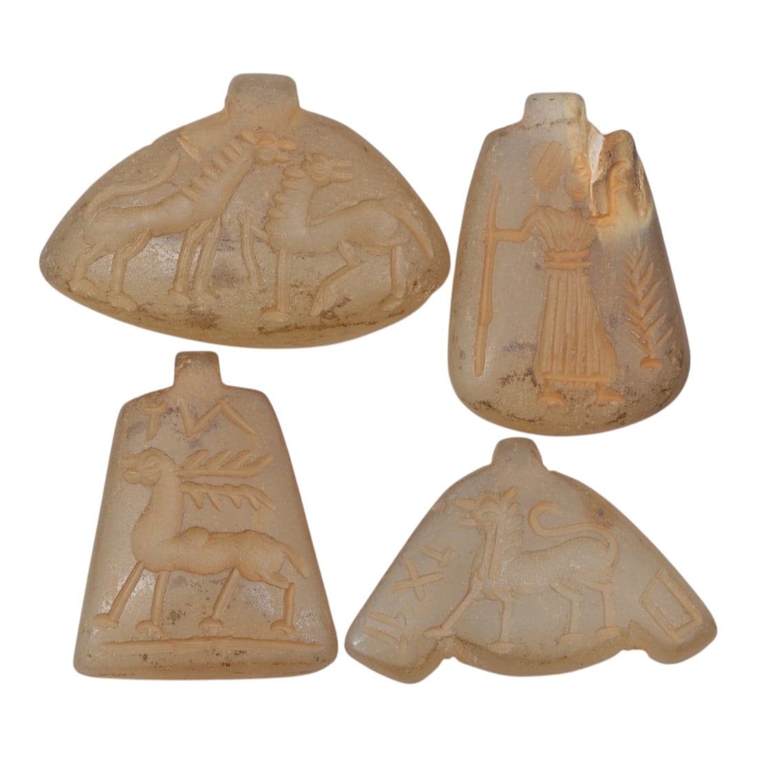 Lot of 4 Ancient Chalcedony Amulet Pendants, 56WM: A collection of four ancient amulet pendants, expertly carved from translucent chalcedony stone. Each pendant features a suspension loop at the top and is engraved with distinct motifs: confronting an