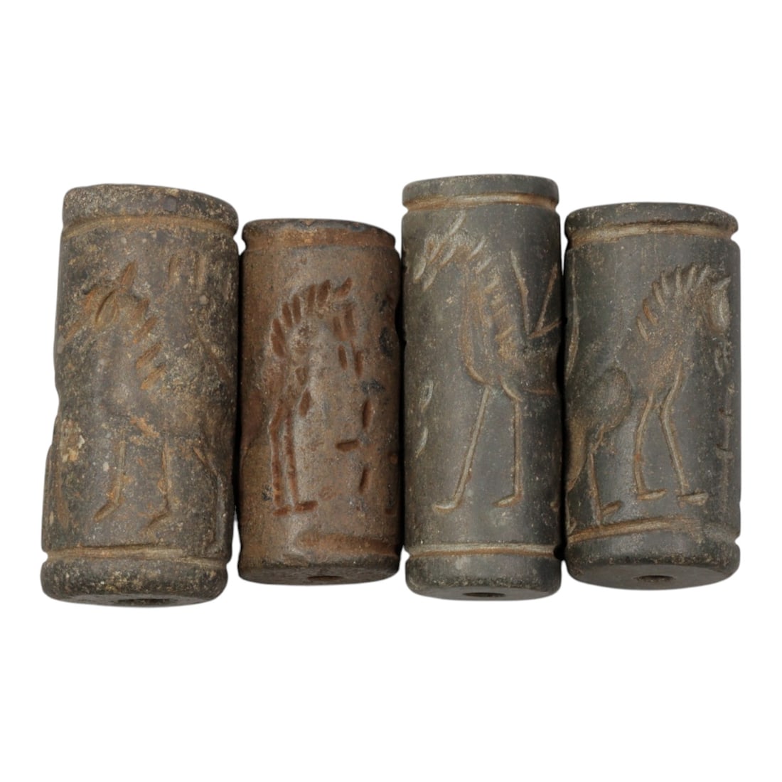 Lot of 4 Ancient Mesopotamian Cylinder Seals, 96WM: A curated lot of four ancient Mesopotamian-style cylinder seals, carved from dark stone with natural patination and wear consistent with age. Each cylindrical seal features a central perforation for u