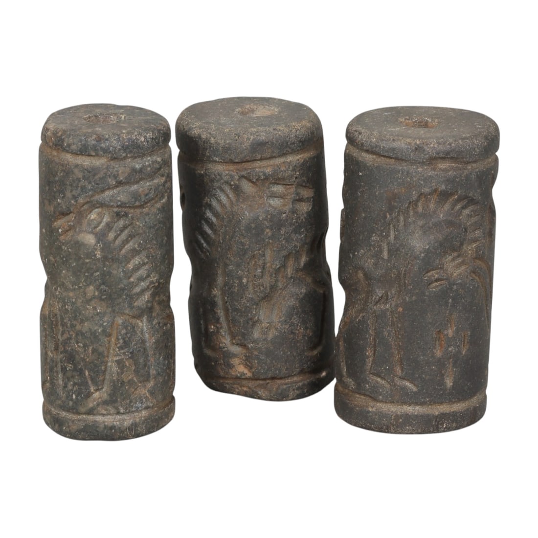 Lot of 3 Ancient Mesopotamian Cylinder Seals, 48WP: A curated lot of three ancient Mesopotamian-style cylinder seals, carved from dark stone with natural patination and wear consistent with age. Each cylindrical seal features a central perforation for 