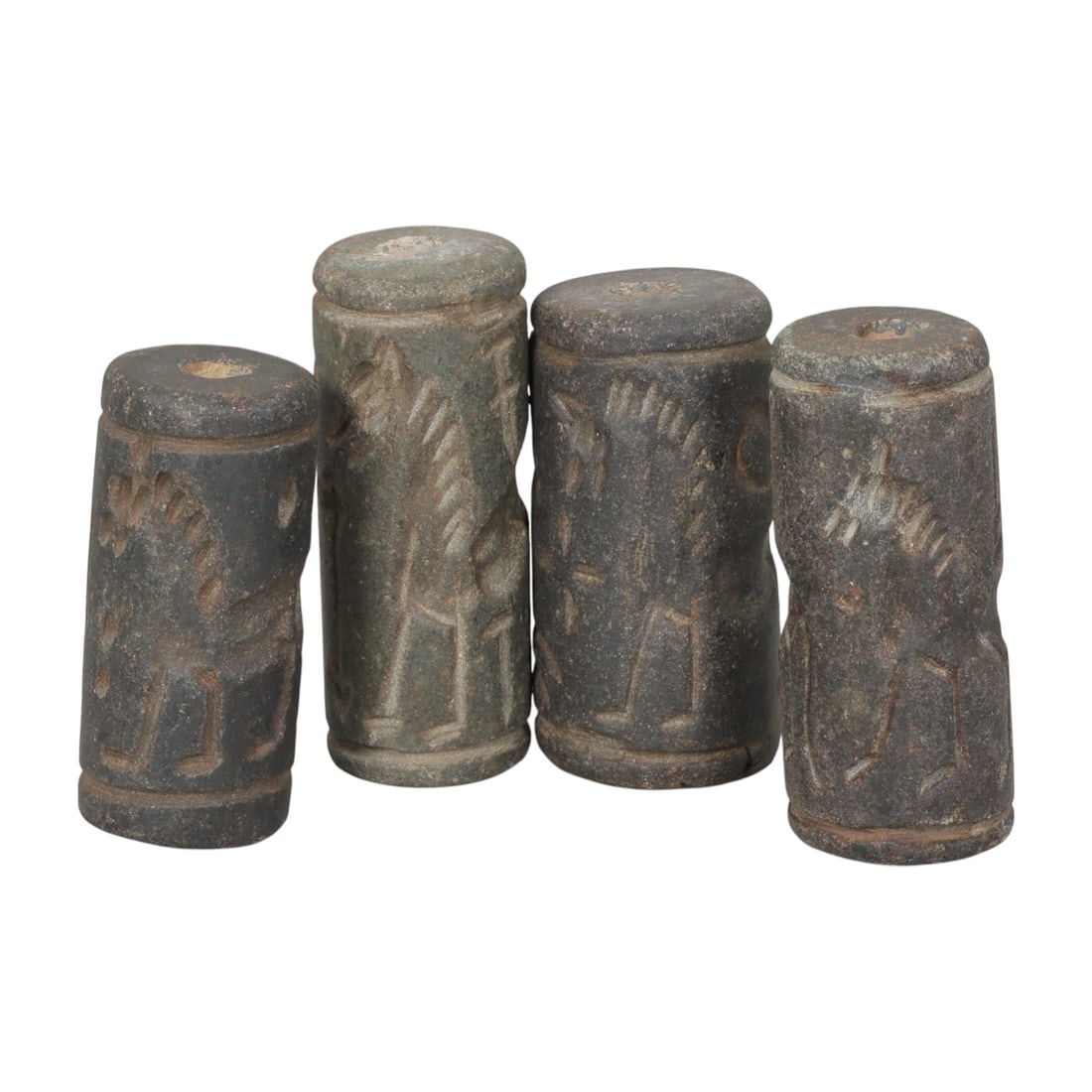 Lot of 4 Ancient Mesopotamian Cylinder Seals, 50WP: A curated lot of four ancient Mesopotamian-style cylinder seals, carved from dark stone with natural patination and wear consistent with age. Each cylindrical seal features a central perforation for u