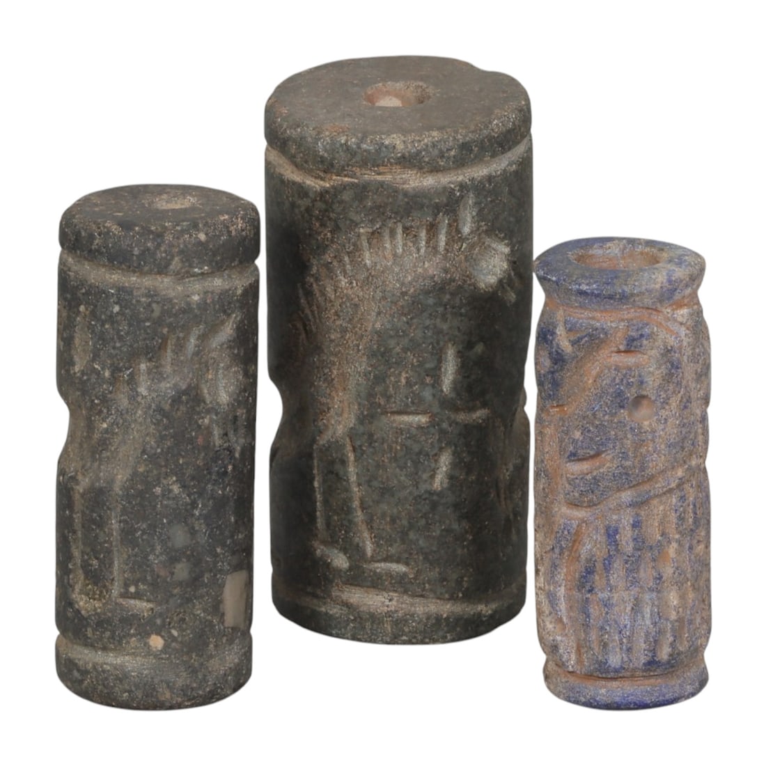 Lot of 3 Ancient Mesopotamian Lapis Lazulli Cylinder Seals, 49WP: A curated lot of three ancient Mesopotamian-style cylinder seals, including two carved from dark stone and one from lapis lazuli. Each cylindrical seal features a central perforation for use with a ro