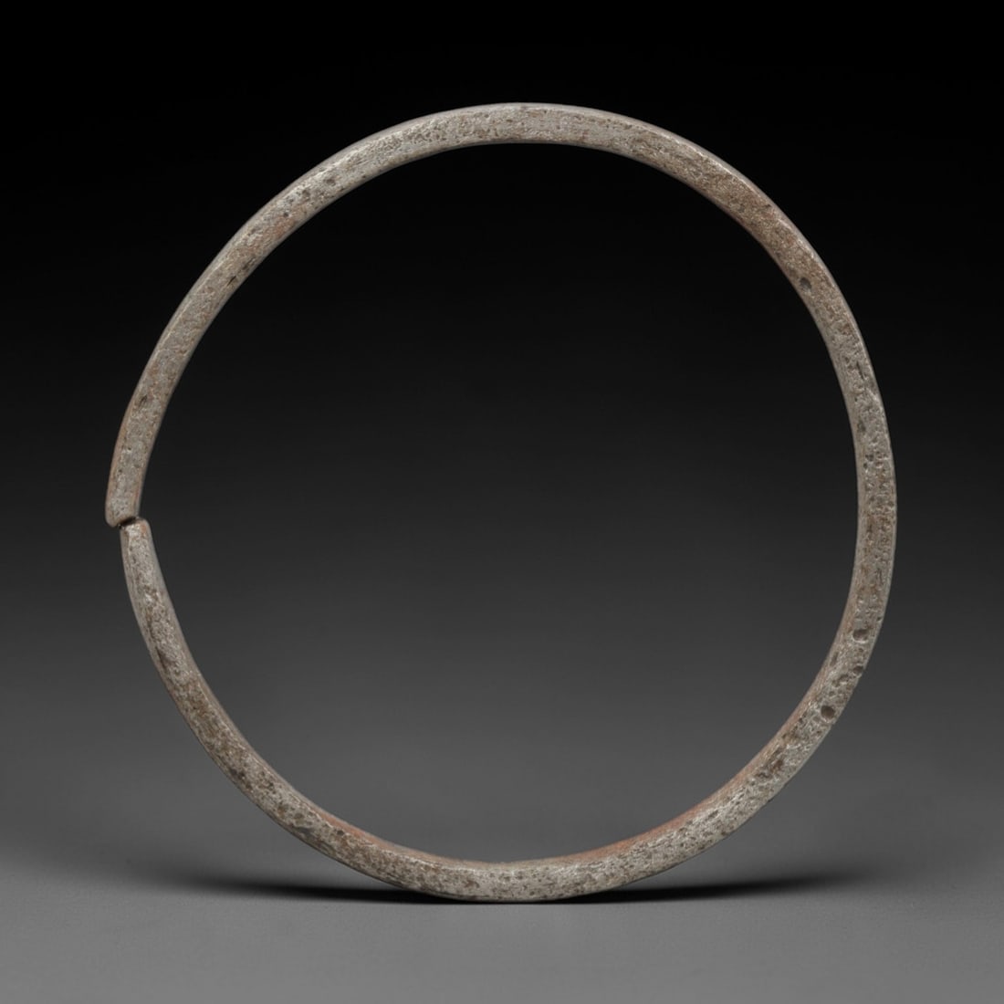 A Celtic Iron Penannular Bracelet, 2nd Century BCE - 1st Century CE, 5FV: Forged from iron with a consistent, slender rounded section, the bracelet is formed as a classic penannular ring with a neat, narrow terminal gap and straight, unadorned ends. The surface bears a dens