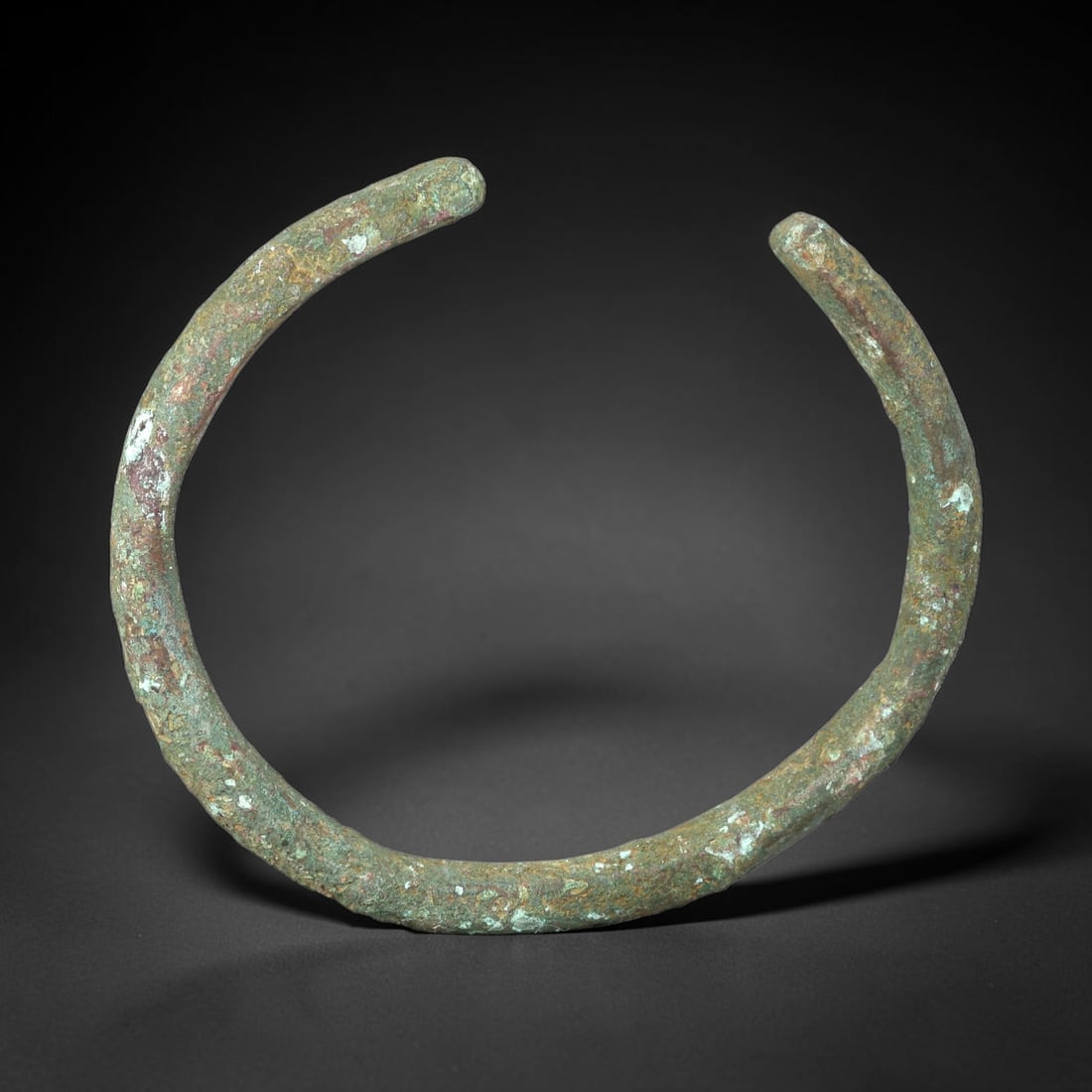 Ancient Bronze Bracelet - Roman Open Cuff Bangle, 44BN: An open-form bracelet crafted from cast bronze, with a rounded cross-section and simple rounded terminals. The robust form is characteristic of utilitarian Roman provincial jewelry, designed for durab