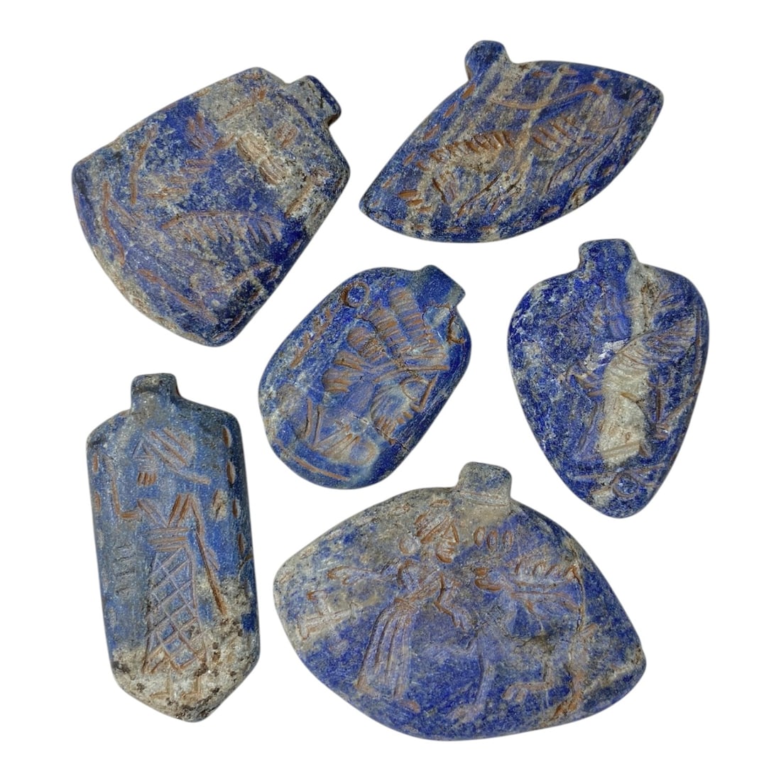A Lot of 6 Ancient Near Eastern Lapis Lazuli Amulets, 7AC: The group comprises six amulets carved from lapis lazuli, exhibiting rich blue tones with natural white and grey mineral inclusions, alongside surface patina and wear consistent with ancient use. Each