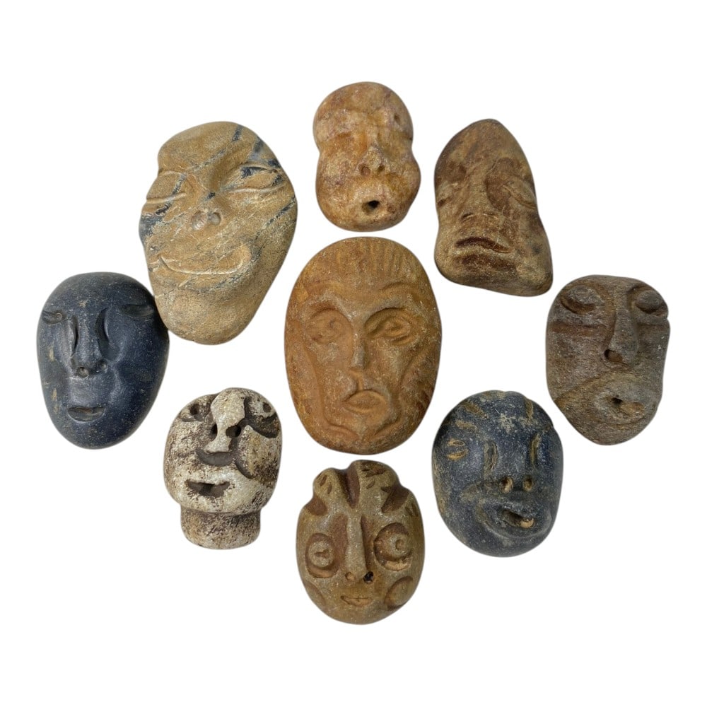 A Lot of 9 Ancient Medieval Stone Maskette Amulets, 2AB: The group comprises nine carved stone maskette amulets, each depicting stylized human or zoomorphic faces. The pieces vary in detail, from deeply defined facial features to more schematic renditions, 