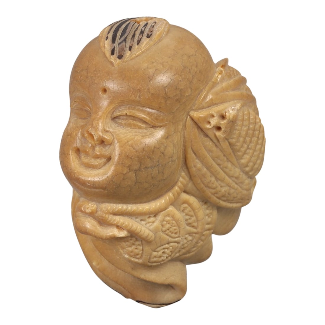 An East Asian Carved Head Ornament, 20th Century, 95FC: Carved from a light brown to ochre-toned material of uncertain composition, the object is worked in the form of a stylized human head shown three-quarter view. The face is rounded with softly modeled 