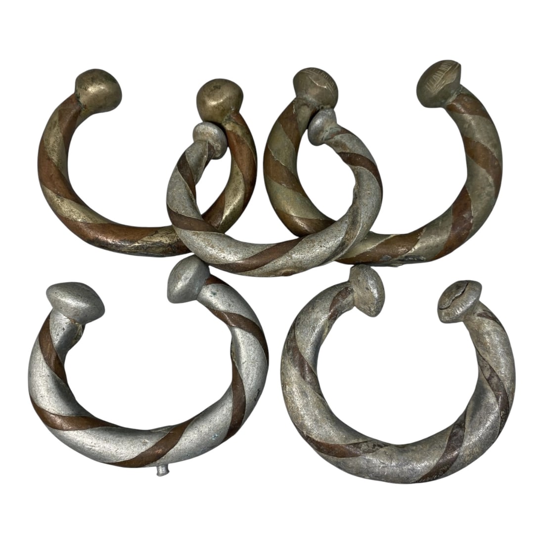 Lot of 5 Antique African Copper Alloy Bracelets, 60AG: The group consists of five C-shaped bracelets crafted from copper alloy with contrasting metal inlay. Each bracelet features a twisted, striped pattern of silver-toned and copper-toned metal bands, te