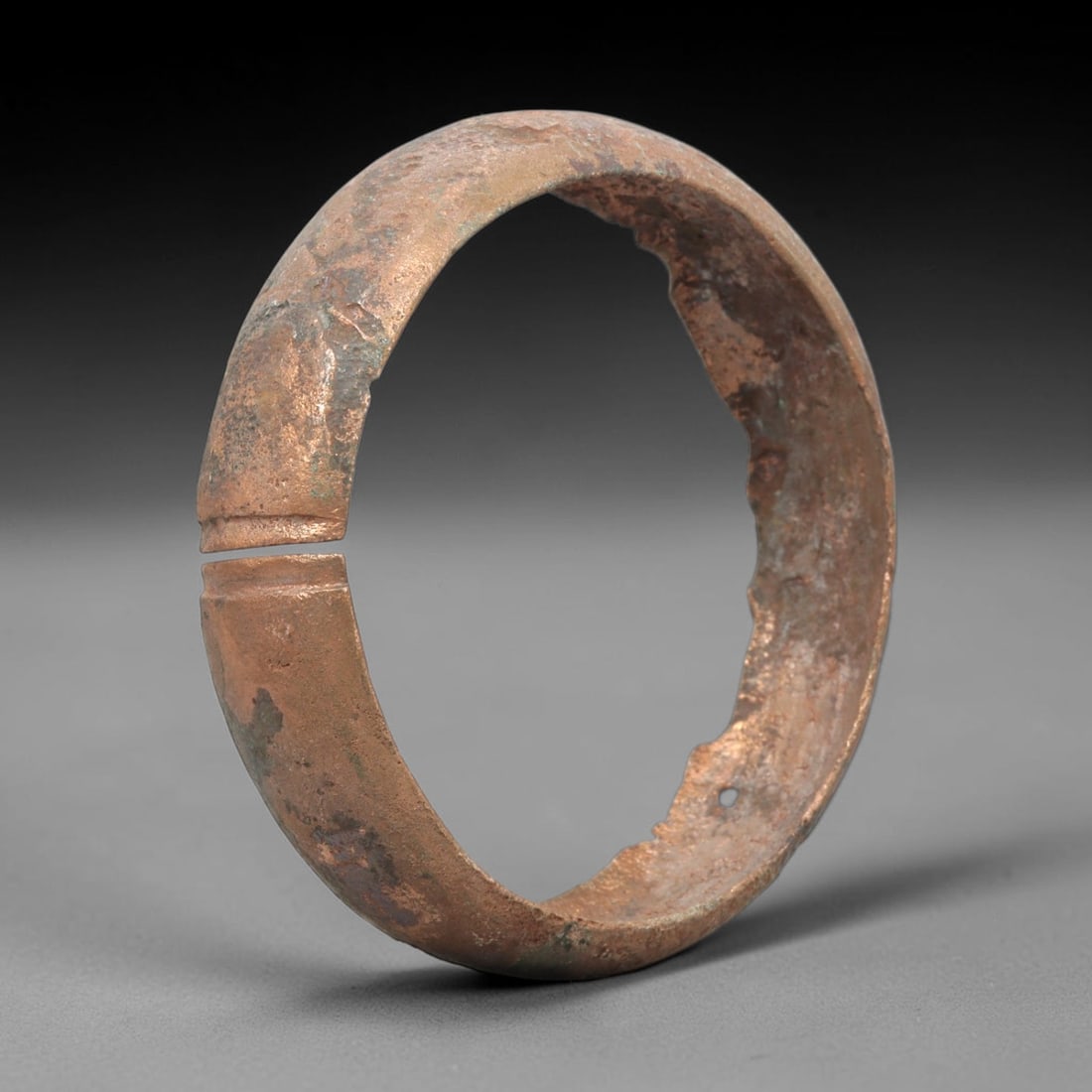 Ancient Roman Bronze Bracelet - Split Form, 22BN: Crafted from bronze, this open bracelet features a wide, flat hoop form with a distinct split and decorative linear incisions at the terminals. The surface retains a warm, coppery patina with scattere