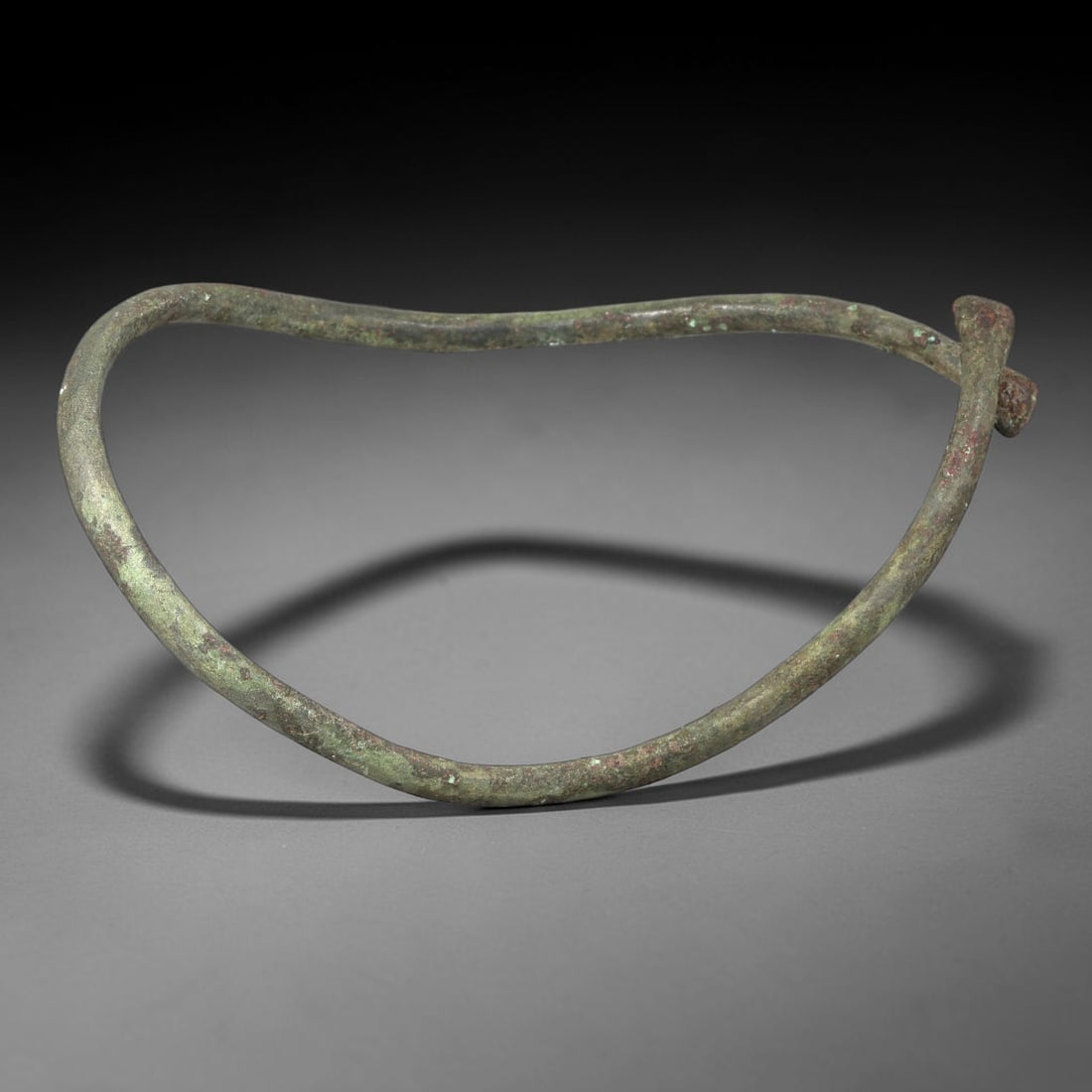 Ancient Bronze Anklet - Roman Penannular Bangle, 97BN: A penannular bronze anklet of ancient Roman origin, formed from a slender, rounded bronze band. The piece features a simple toggle closure at one end, characteristic of Roman provincial jewelry constr