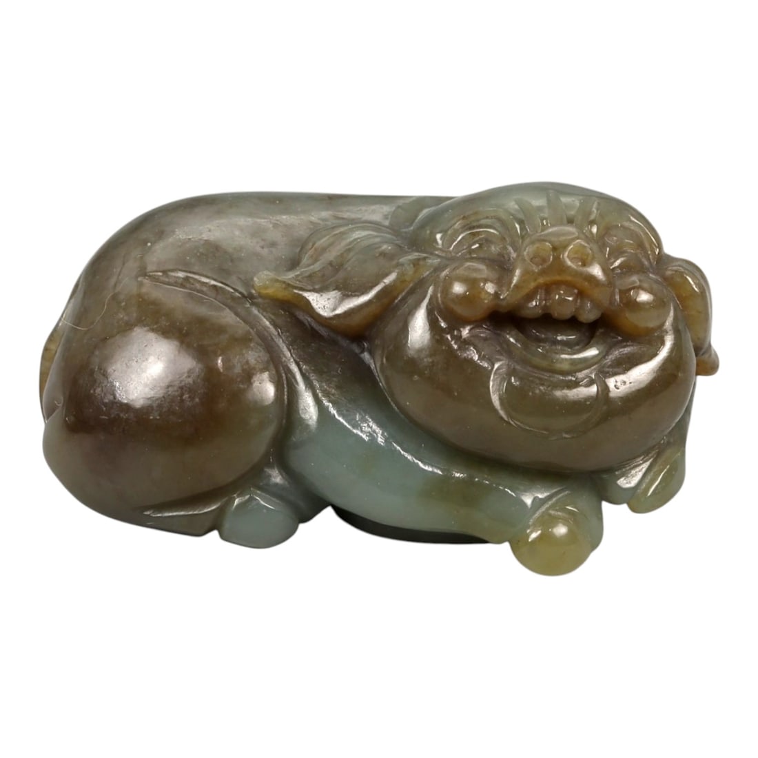 A Chinese Nephrite Jade Pig Figure, 20th Century, 69FB: Carved from mottled grey-green and brown nephrite jade with areas of natural translucency, the figure represents a recumbent pig rendered in a compact, rounded form. The body is modeled in the round w
